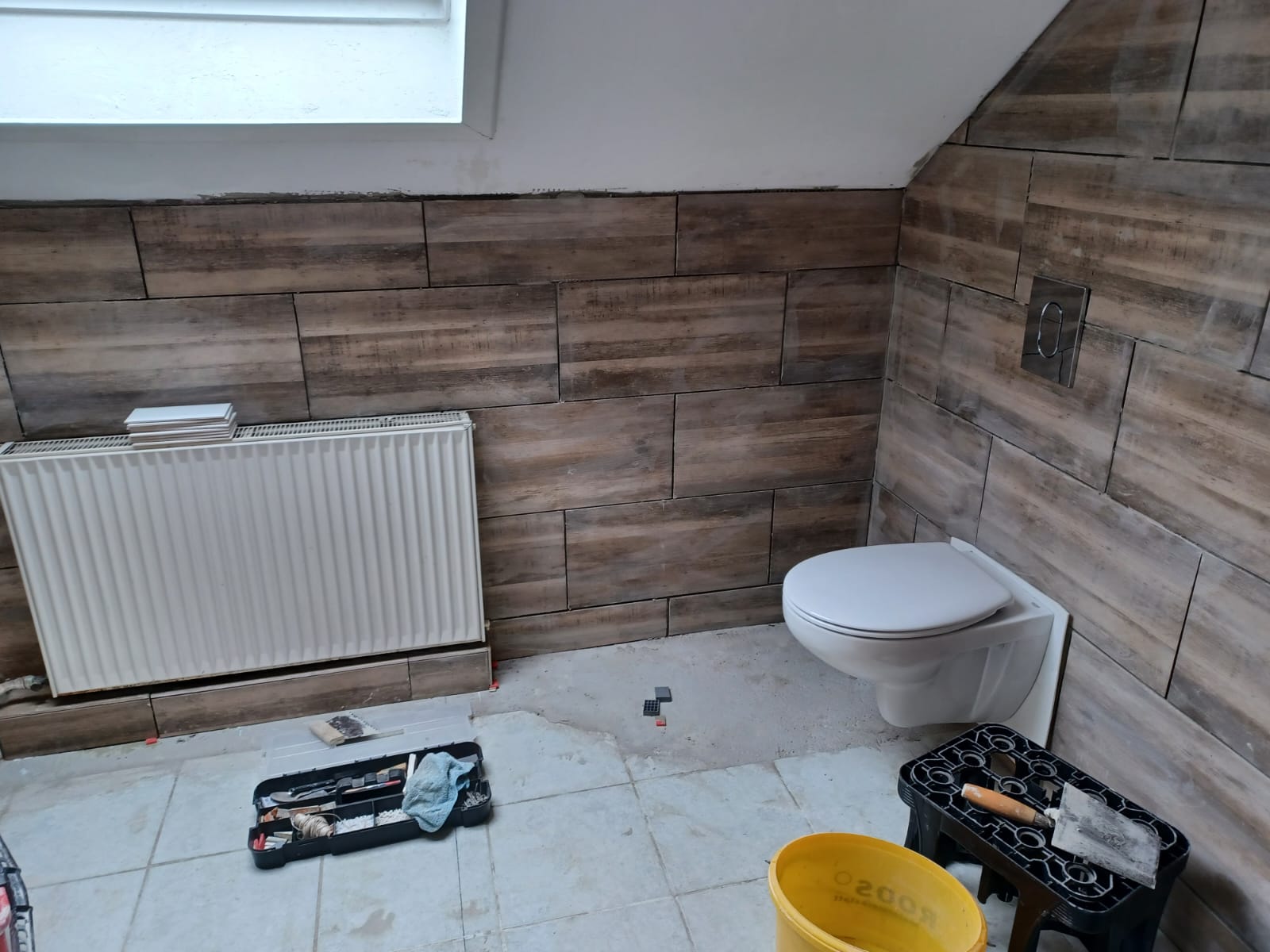 Wandfliesen in Holzoptik hinter Toilette und Heizkörper während der Badrenovierung